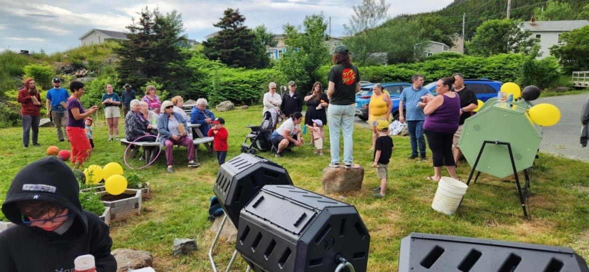 Group of people sit and stand in a garden to kick off the Beauline composting program. There's some balloons and big compost bins.