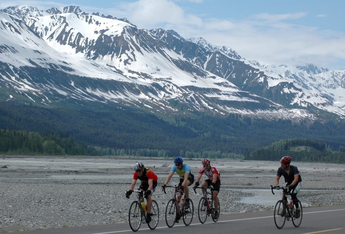Cyclists racing on a road through snowy mountains.