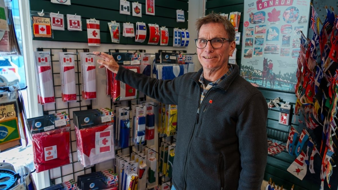 brad-green-world-of-maps-ottawa-canadian-flag-canada A man stands in front of flag merchandise.