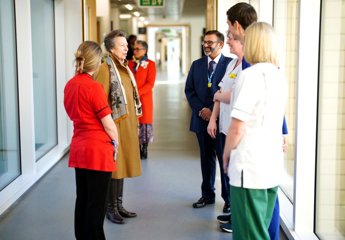 Several people stand and talk in a hallway with large windows down each side.