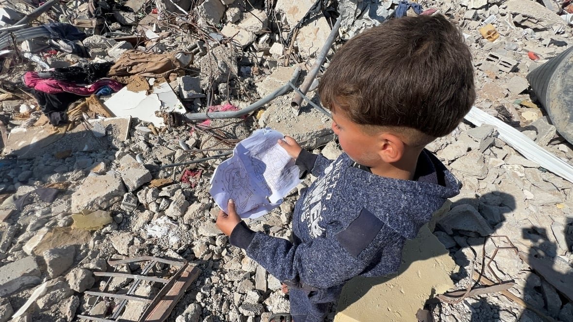 A young boy holds up some colouring paper atop the rubble.