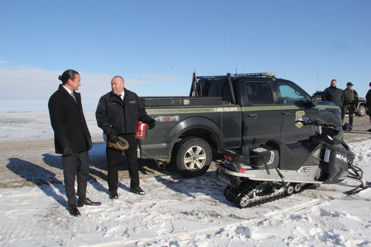 conservation-officers-announcement Two men standing in front of a truck and a snowmobile.