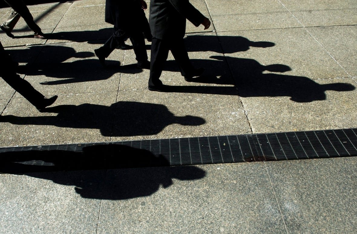 Shadows of men in suits are seen against the pavement.