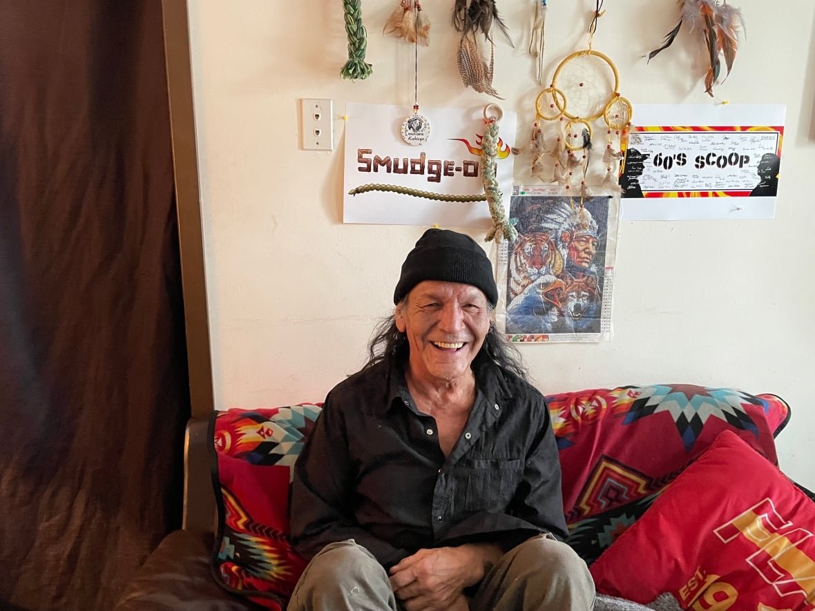 Man sits on a couch with dreamcatchers on the wall