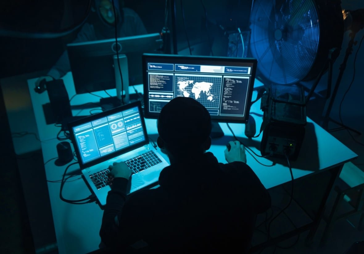 hacking-stock-generic A man looks at blue-tinted screens with a large fan next to him.