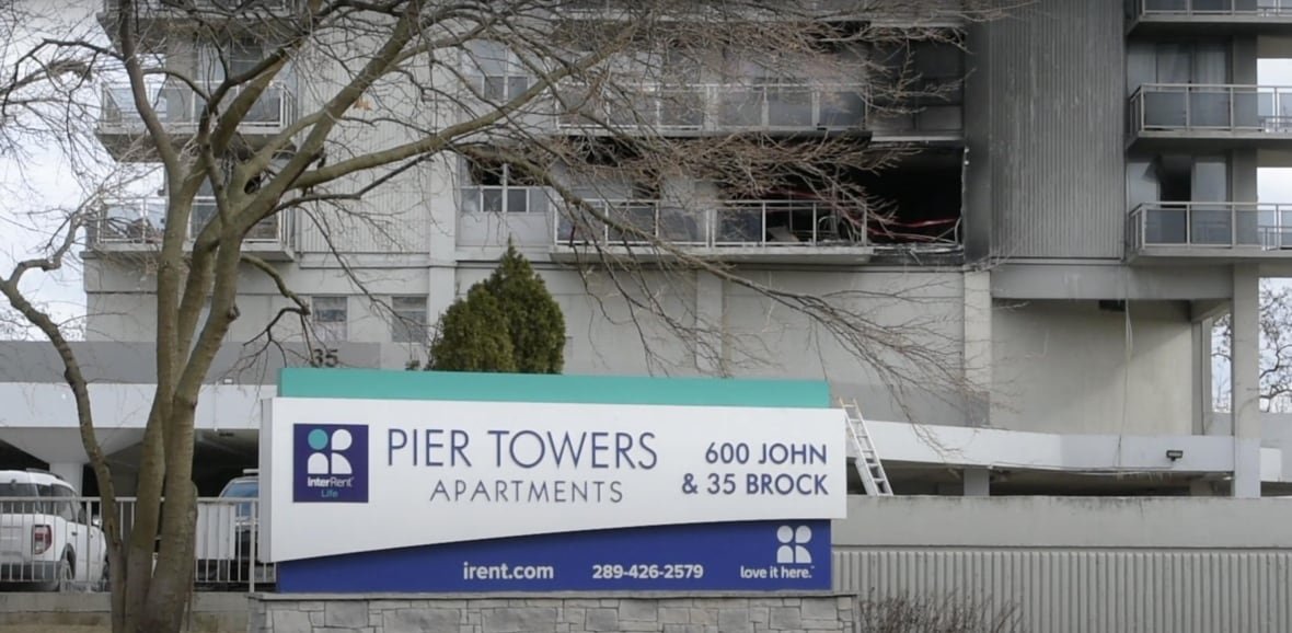 An apartment building sign in front of a building with at least one unit completely destroyed by fire.
