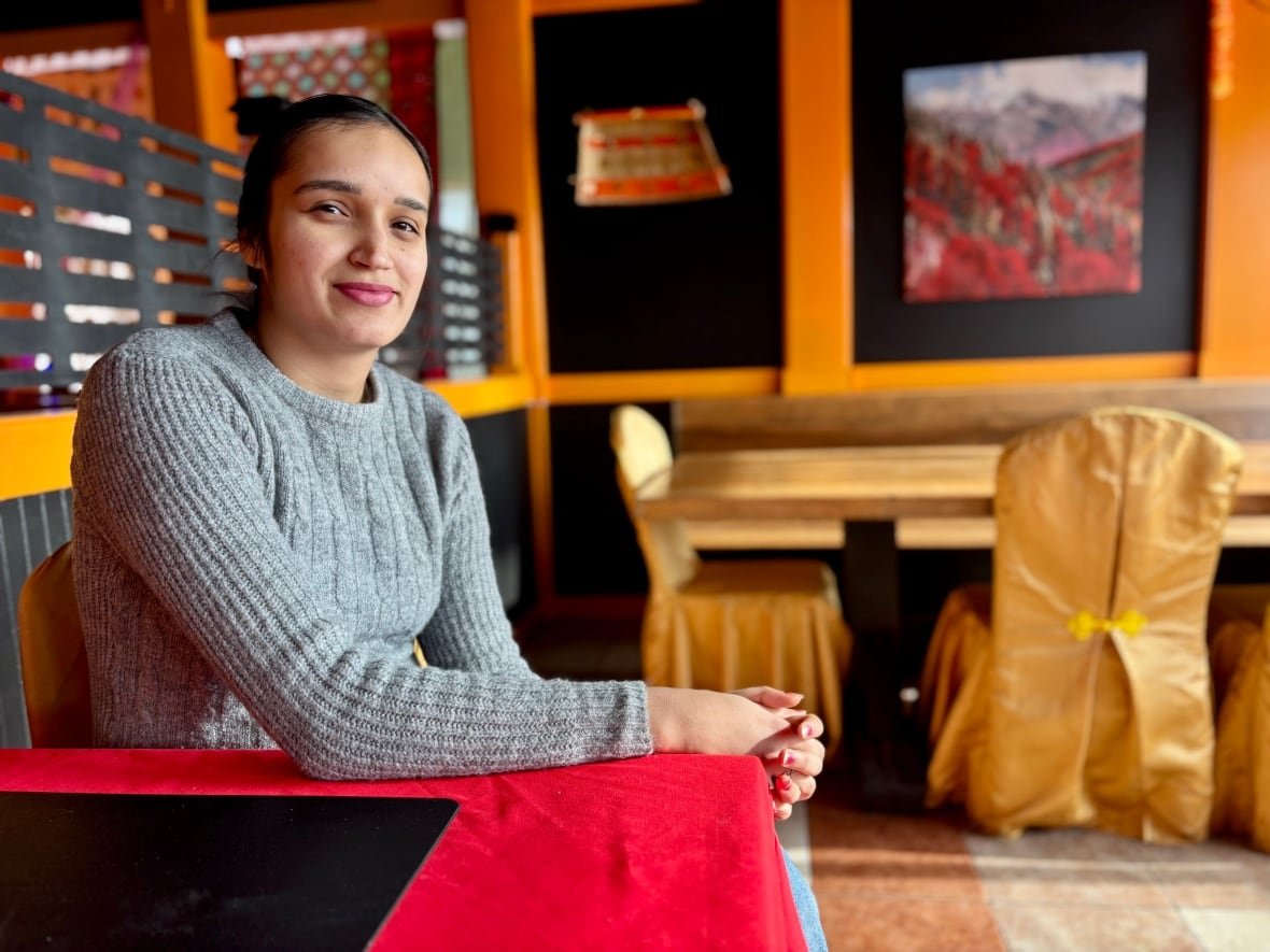 Harneet Brar sits at a table in her restaurant which is covered with a red table cloth. The chairs at the tables have gold covers on them.