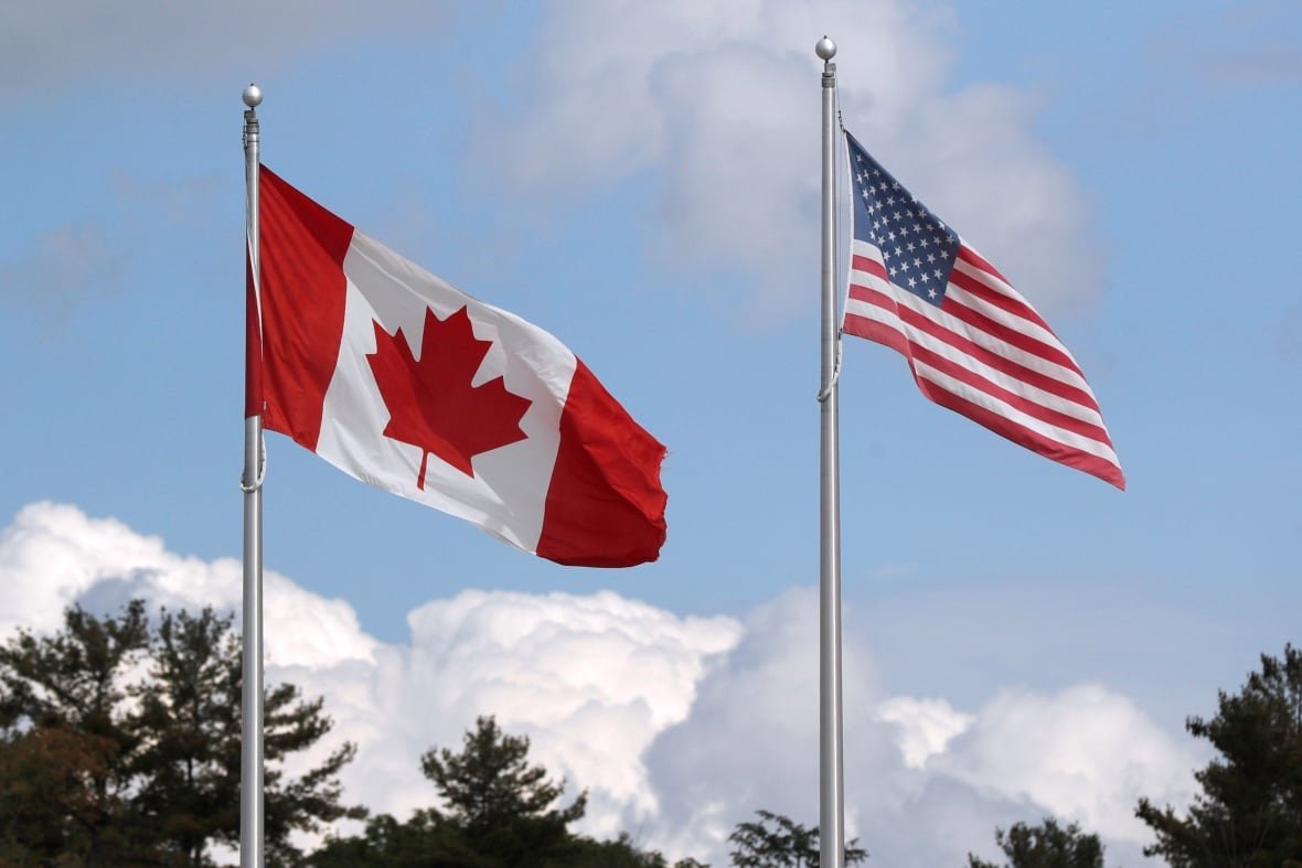 health-coronavirus-usa-canada-1 The American and Canadian flags fly side by side in front of a blue sky.