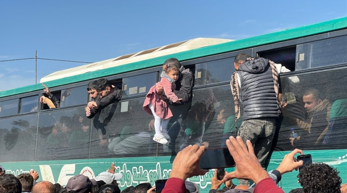 A man in a bus holds a baby while others look outside the vehicle.