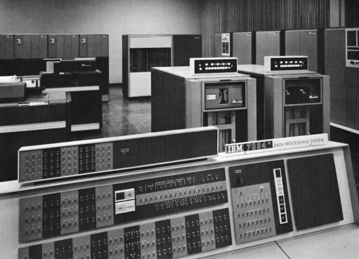 ibm-7094 Big, boxy computers with a lot of switches are seen here in a grainy black and white photograph.