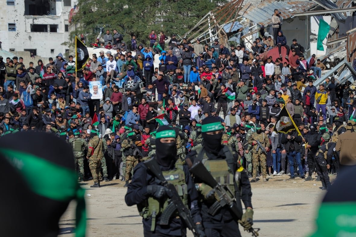 israel-palestinians-8 A crowd gathers behind two masked men carrying rifles.