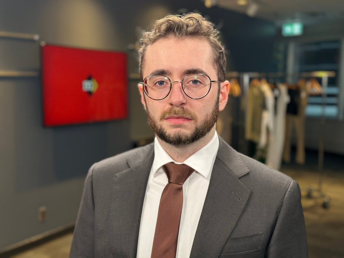 A man in wire rimmed glasses looks at the camera. He is dressed in a suit and tie.