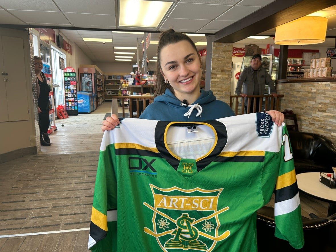 A smiling woman holds out a hockey jersey.