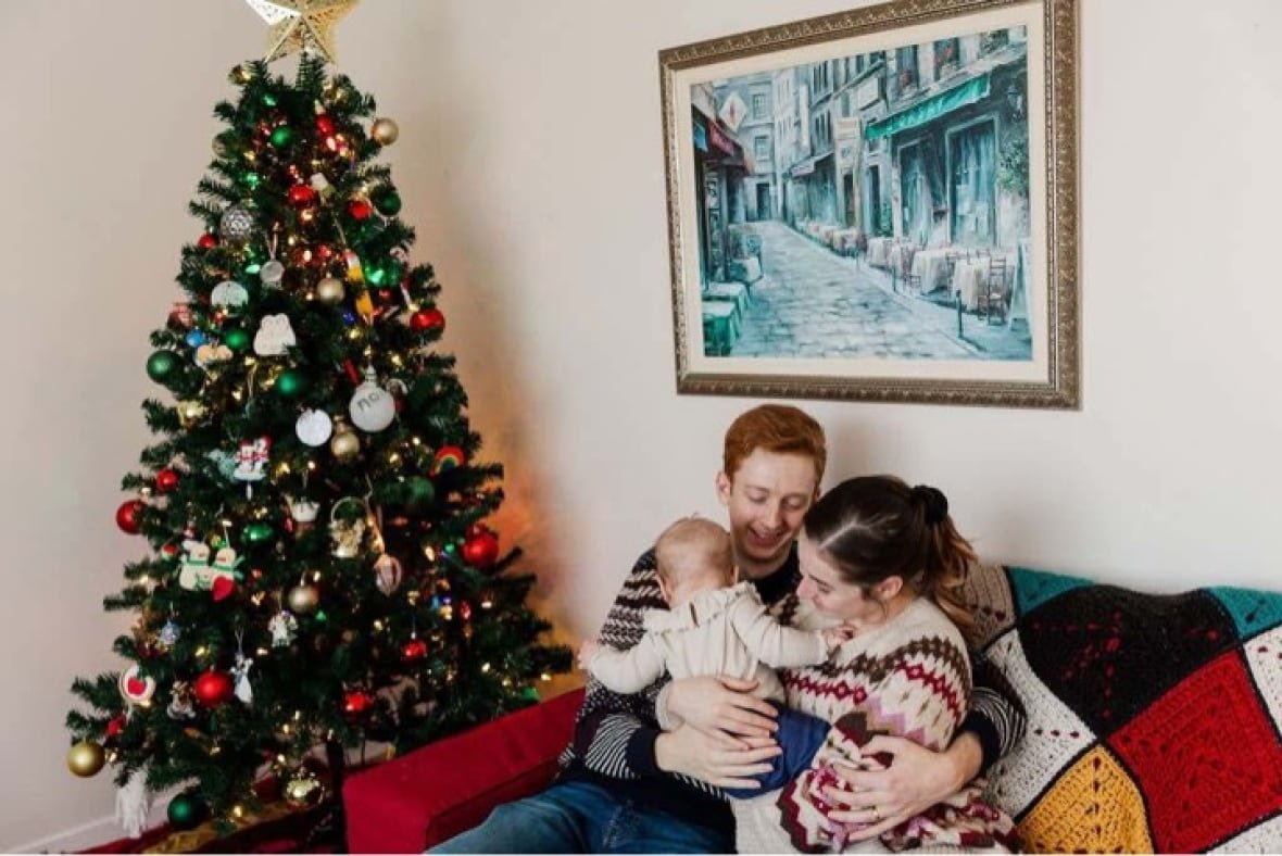 konnor-and-julia-bourgeois A young couple and their baby cuddle on the couch in front of a decorated Christmas tree.