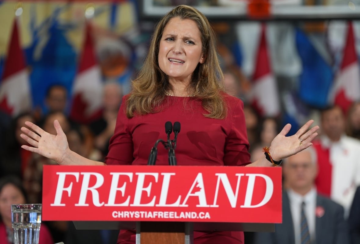 Chrystia Freeland speaks into a microphone at a podium. Behind her are supporters of her campaign.