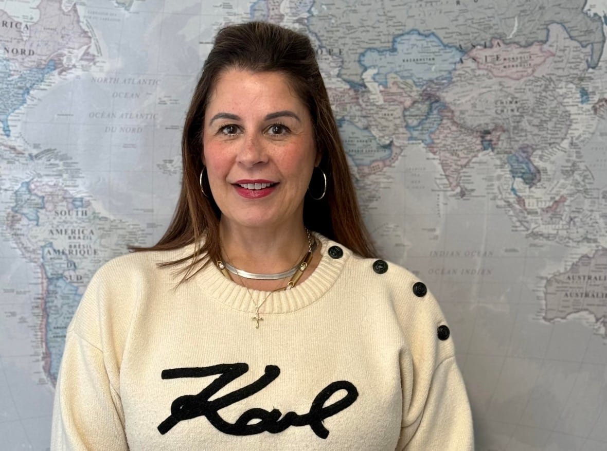 natalie-forrest A woman with brown hair and a beige sweater smiles at the camera with a world map behind her.