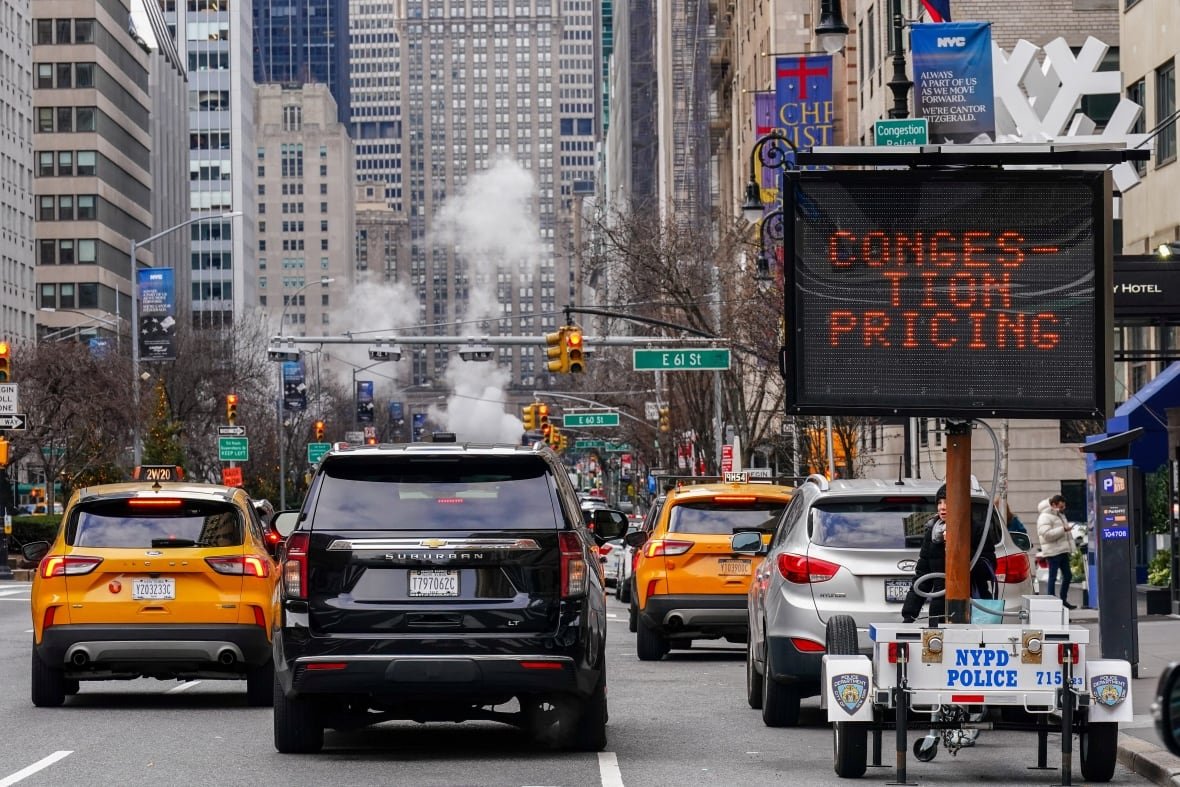 A sign that reads congestion pricing sits on the side of a busy Manhattan road.