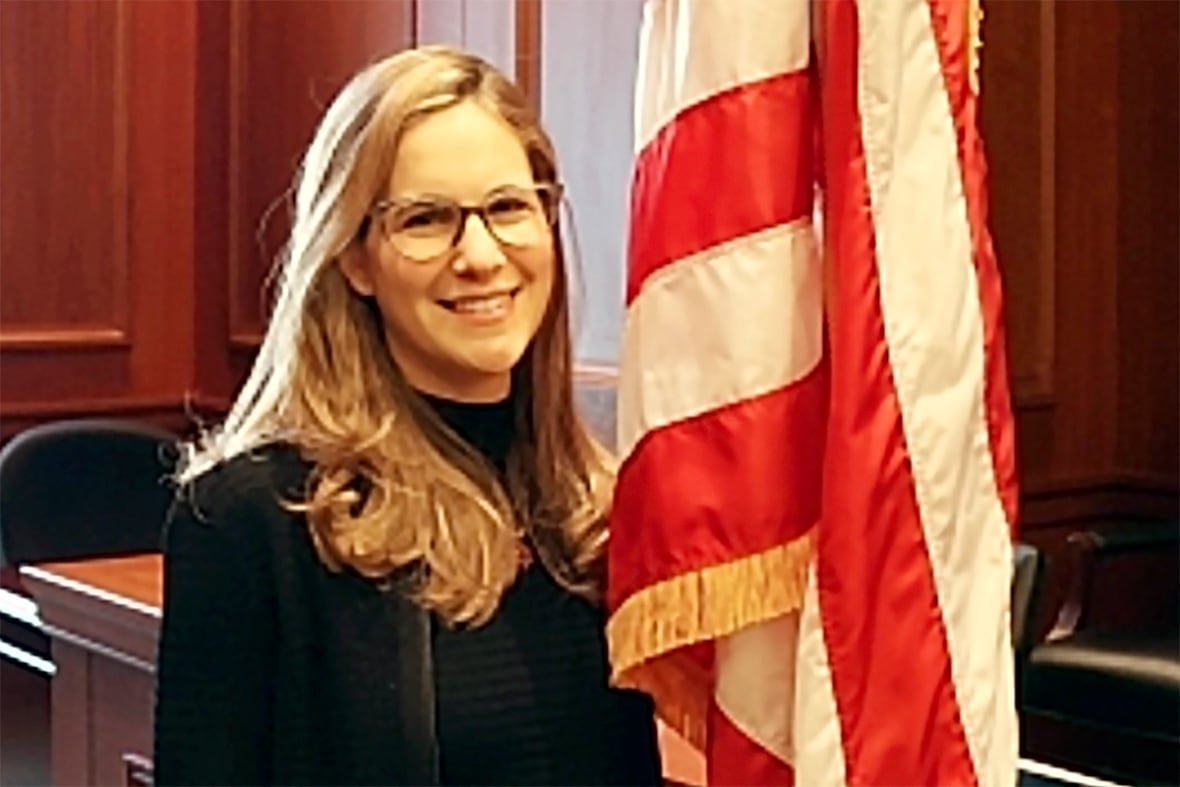 nyc-mayor-investigations-2 A blonde woman in a black blazer and glasses is seen smiling next to an American flag.