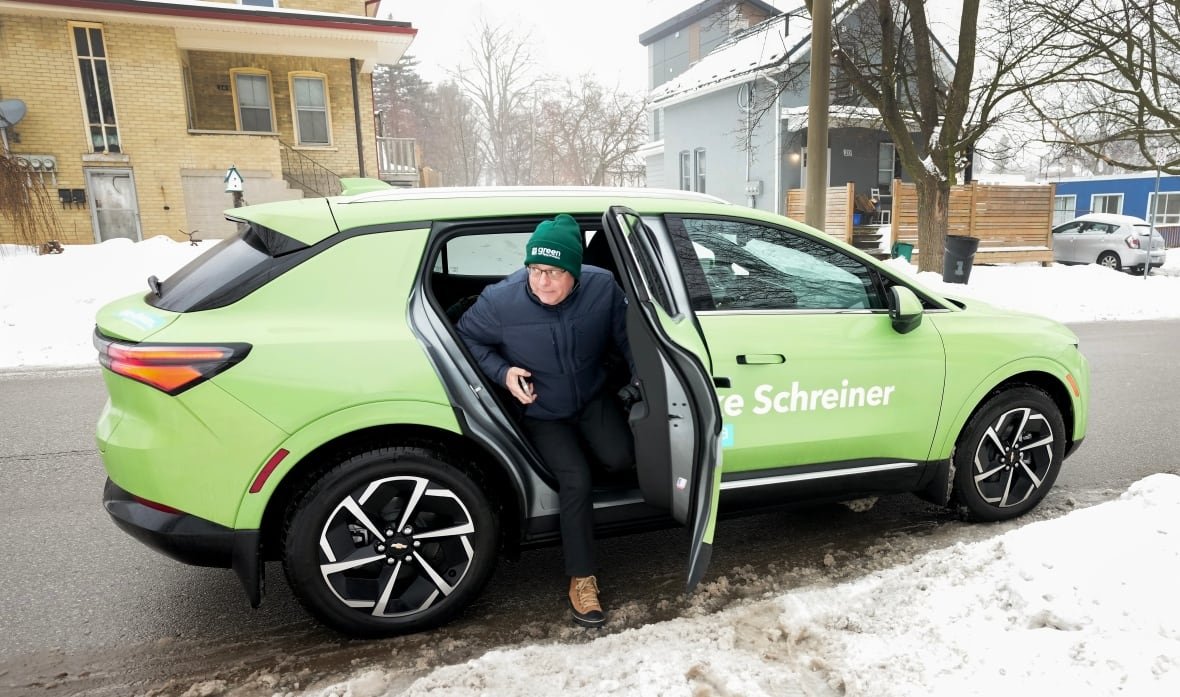ont-elxn-green-party-20250203 Mike Schreiner gets out of the rear of a green-painted electric vehicle, on a snowy street.