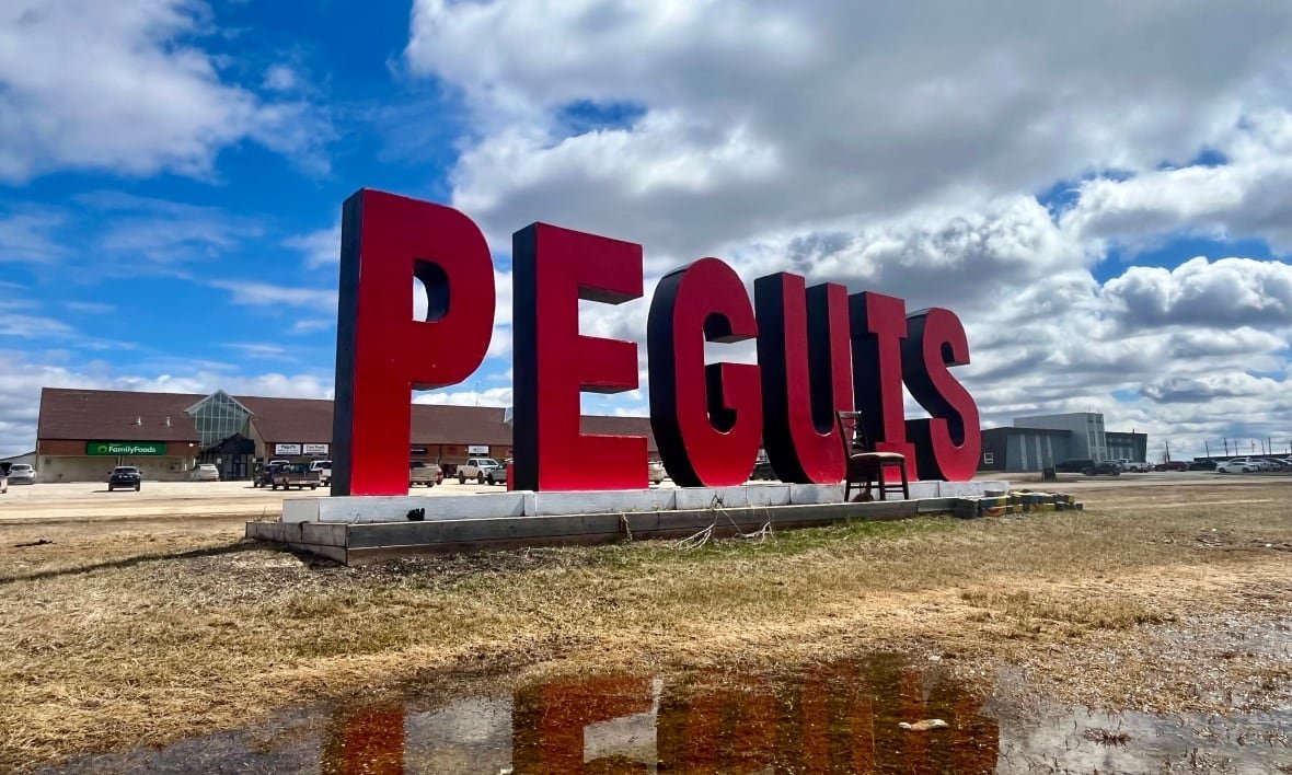 peguis-first-nation The red Peguis sign in front of the Peguis band office, reflected in a puddle.