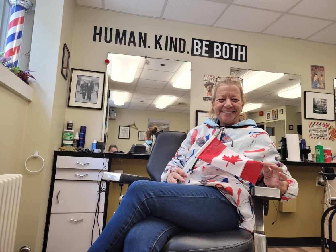 robin-seguin-victoria-barber-shop-ottawa-1 A blonde white woman with glasses on her head sits in a barber chair and looks at the camera.
