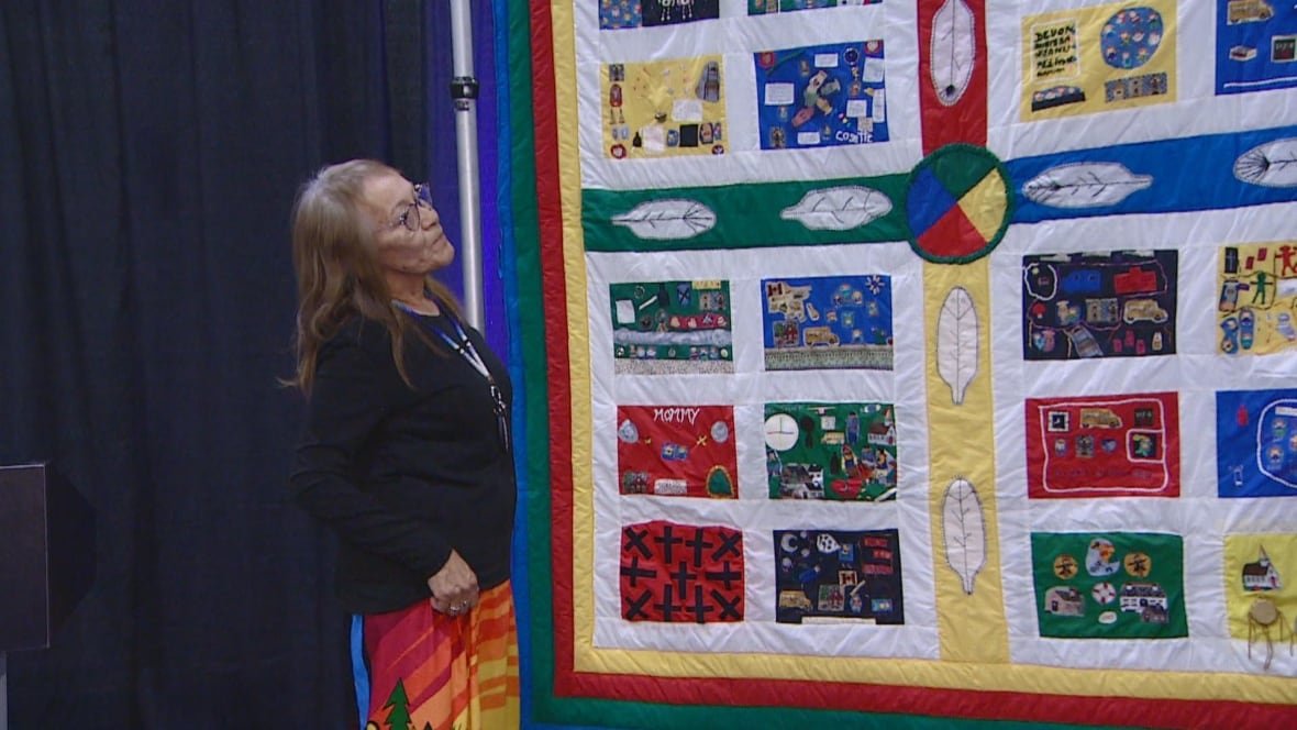 A woman in a colourful stands in front of a bright-coloured quilt