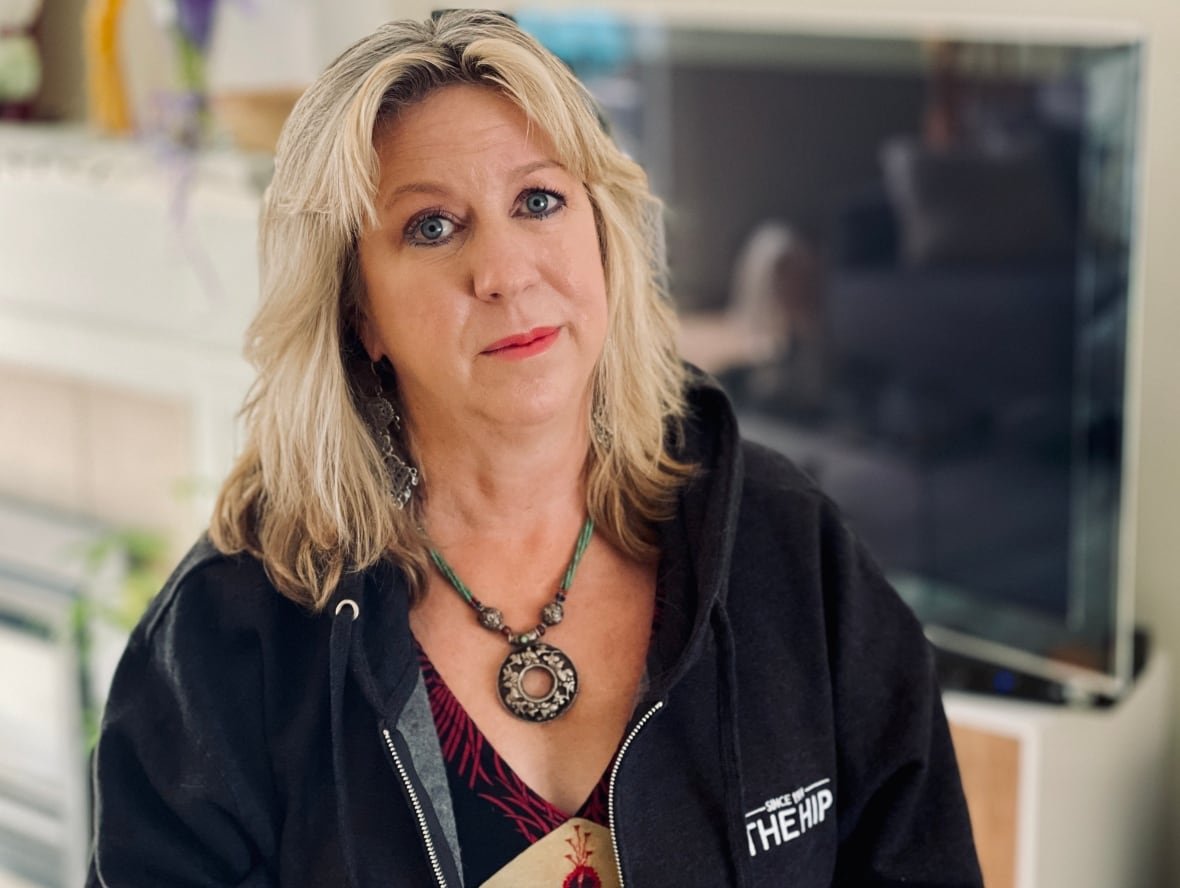 A woman with blond, shoulder length hair wearing a circular pendant and Hip sweater.