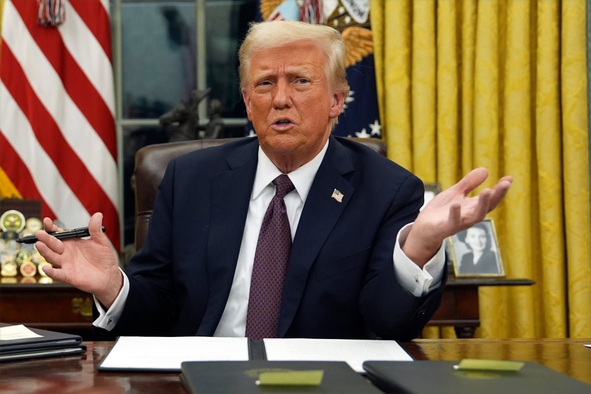 President Donald Trump sits behind his desk and talks to reporters as he signs executive orders in the Oval Office of the White House.