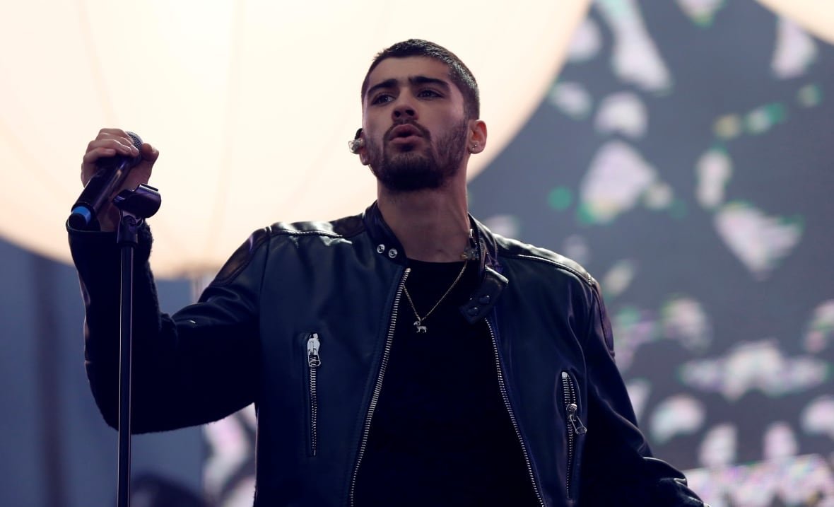 A man in a black leather jacket is seen onstage from the waist up, holding a microphone stand.