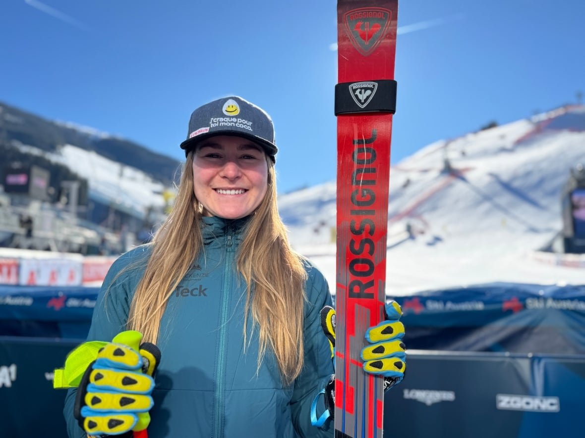 A women's skier standing with her skis held upright in her hand, posing for a photograph in front of the ski hill.