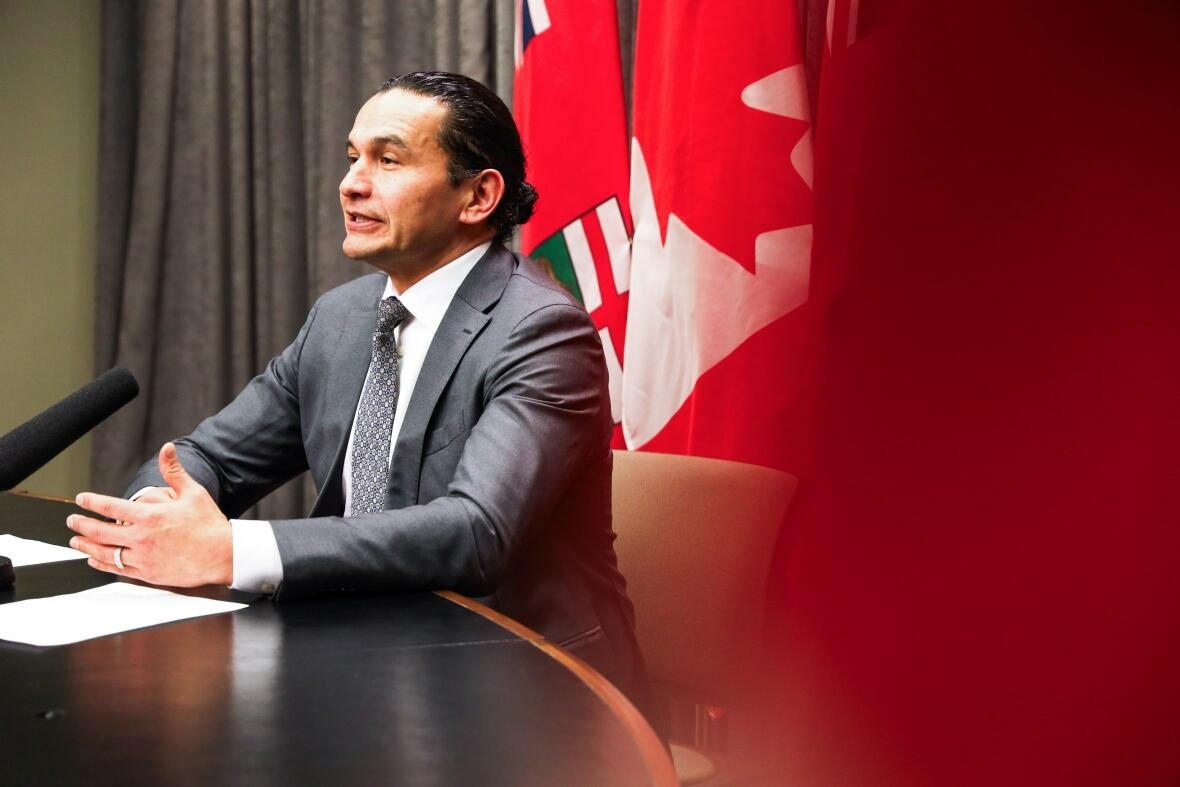 Side view of man speaking behind a desk and gesturing with his hand.