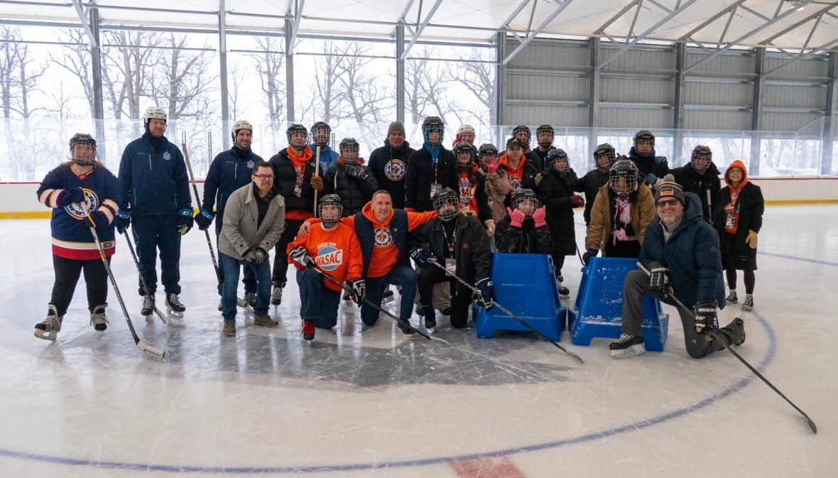 winnipeg-aboriginal-sport-achievement-centre-youth A group of people wearing hockey equipment pose for a photo at the center of a ice rink.