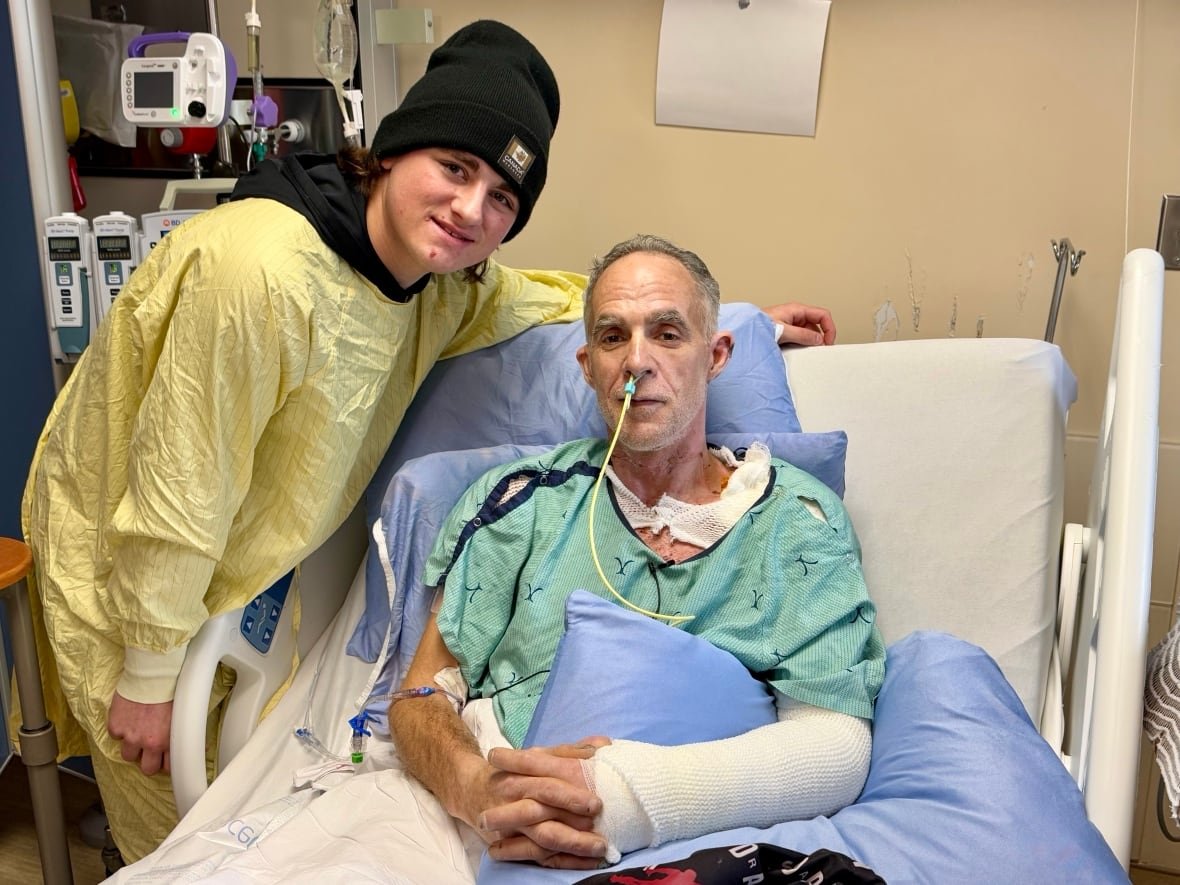zeke-fox-and-shawn-goodwin-1 a teenager in a yellow hospital robe stands next to a man in a bed with a bandaged arm
