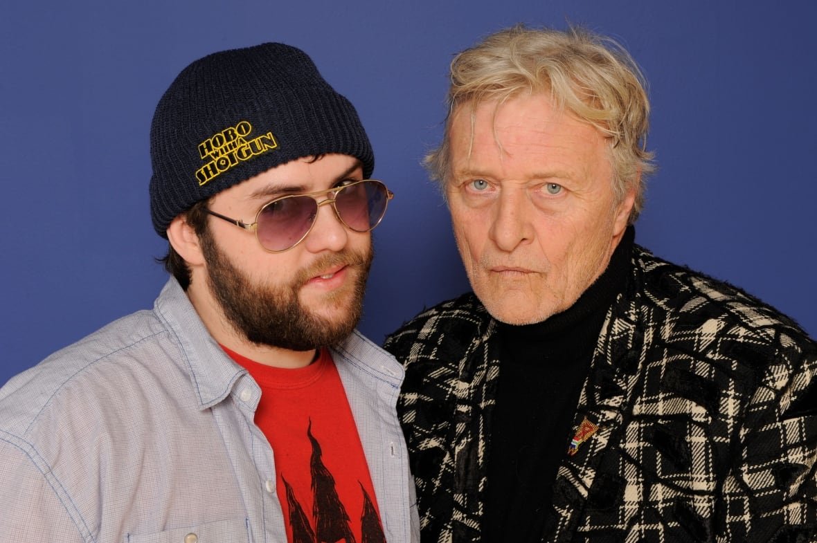 108327582 A filmmaker wearing a tuque that says 'Hobo With a Shotgun' is shown with an actor from the film.