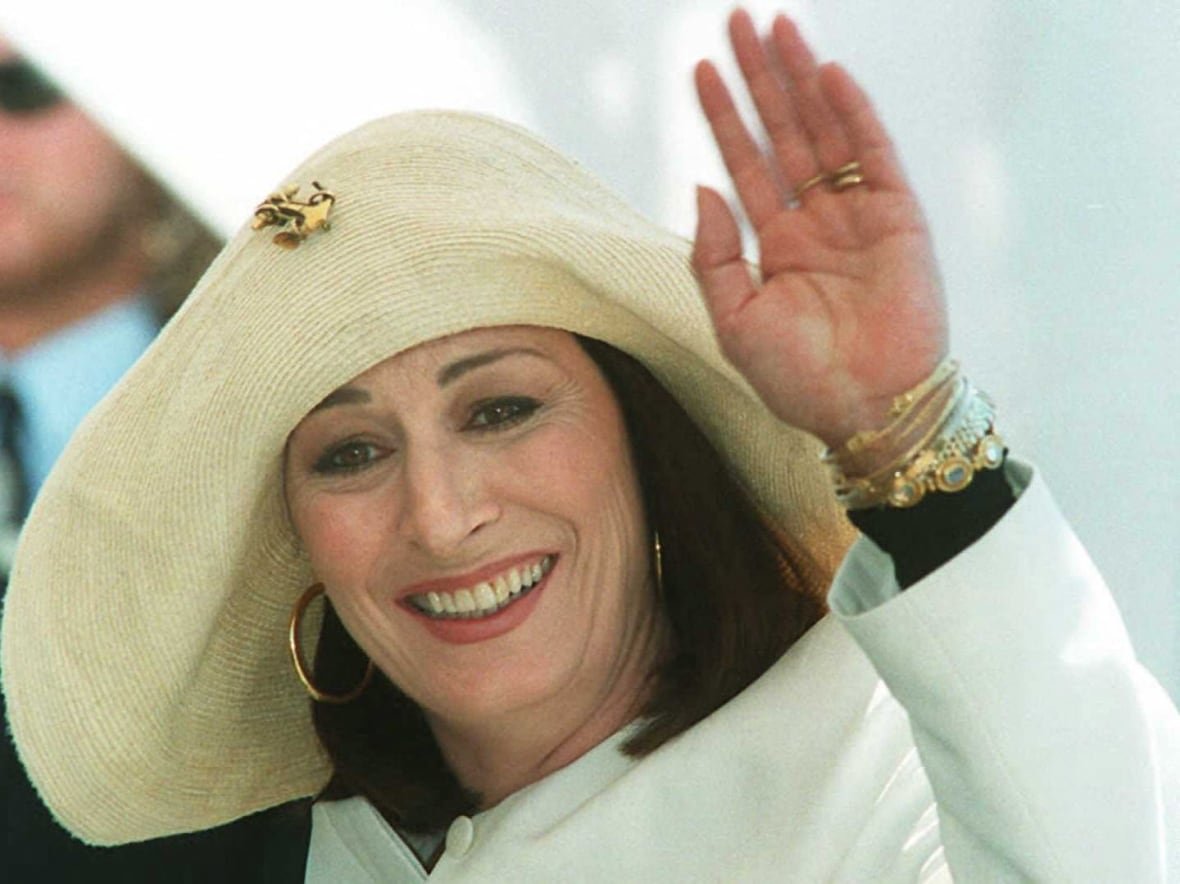 1583554298 A woman wearing a white jacket and a hat waves to photographers.