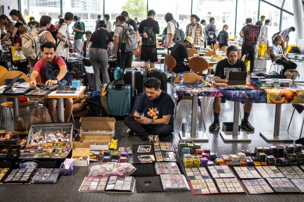 People sit at tables and on the floor with Pokemon products in front of them.