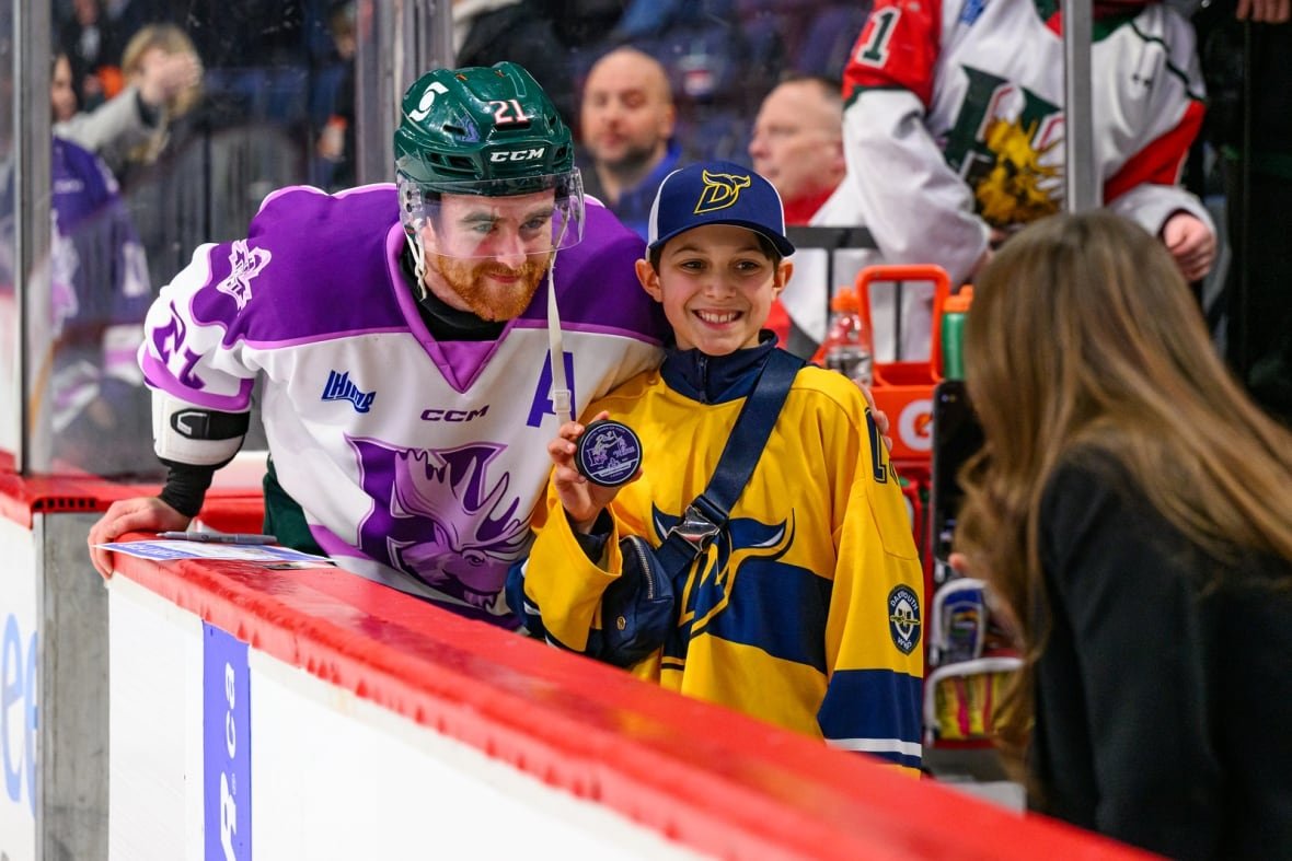 20250208-halvsbat-macphee A hockey player poses with a fan who is showing off a signed puck.