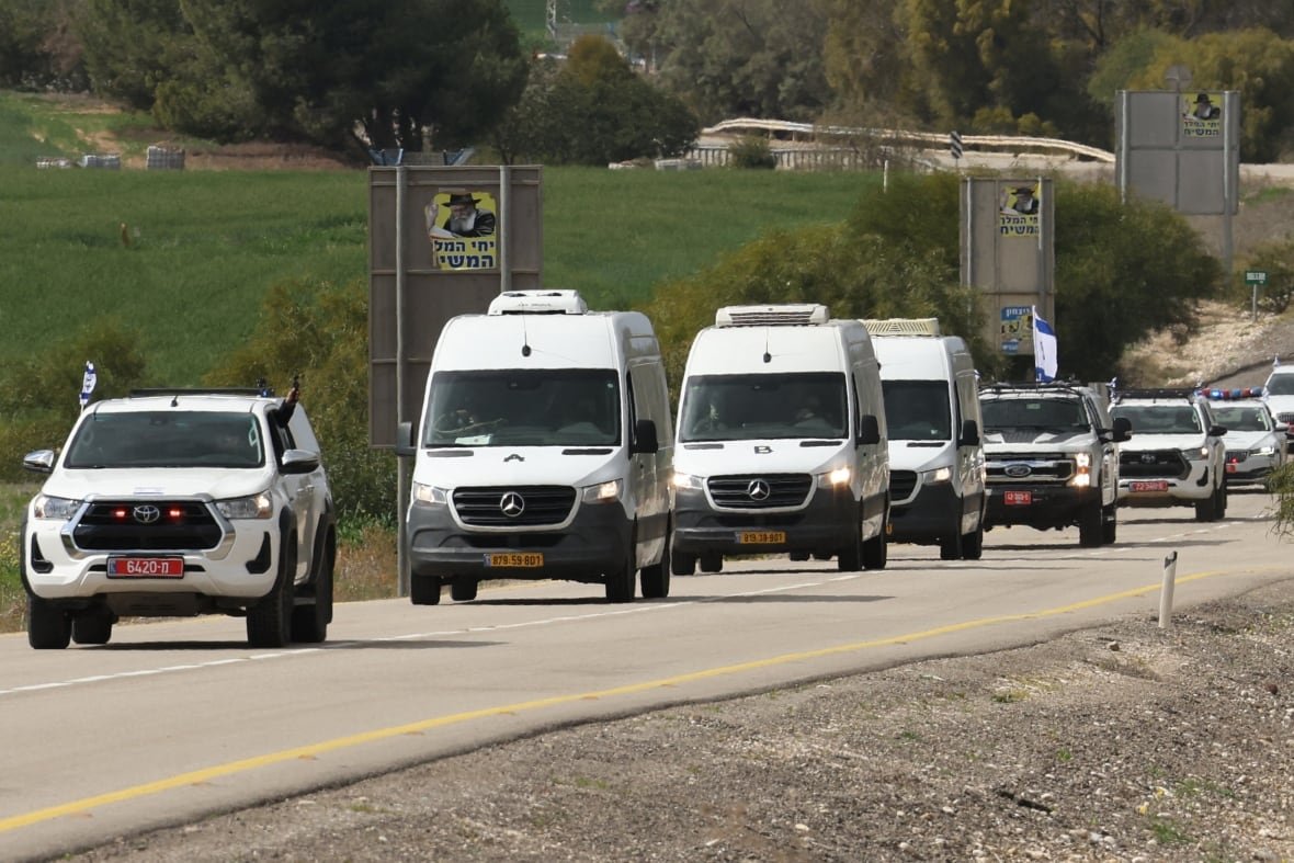 A convoy of white vans, about a half dozen, is shown on a road that appears to be in a rural setting.