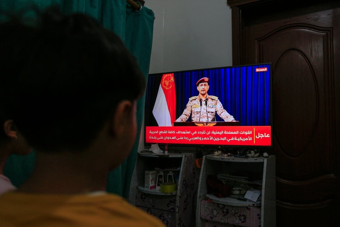 A child watches a television featuring a person in military garb making a speech.