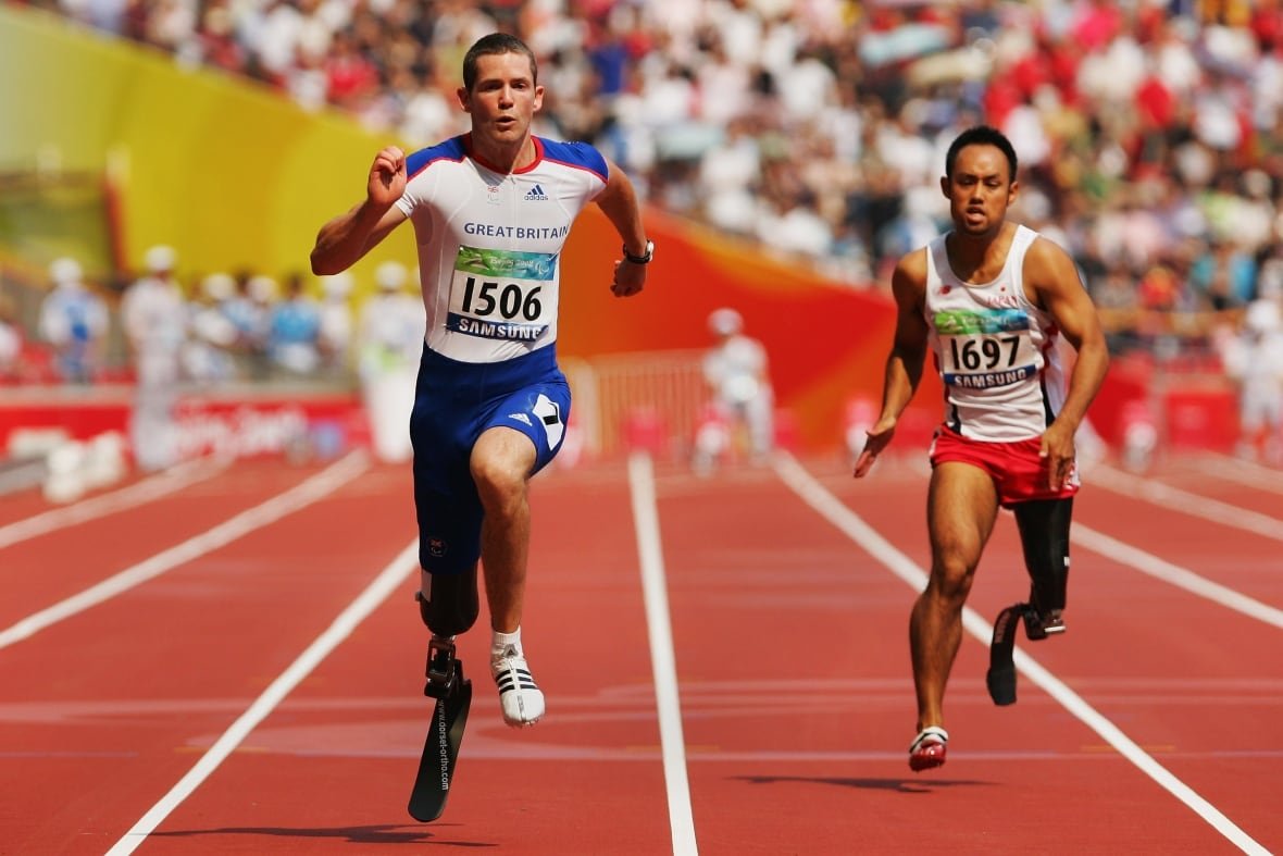 Two men wearing prosthetic legs are running on a track.