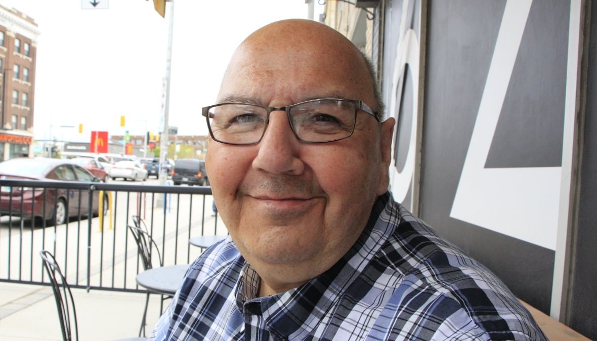 albert-mcleod A man wearing glasses and a blue checkered shirt smiles as he looks toward the camera.