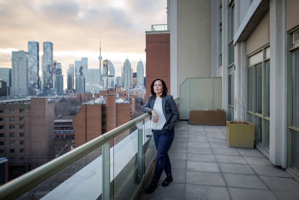 A woman poses  on a balcony overlooking a city skyline
