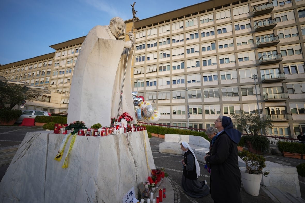 aptopix-vatican-pope-health Nuns kneel to pray at a statue adorned with candles and flowers.