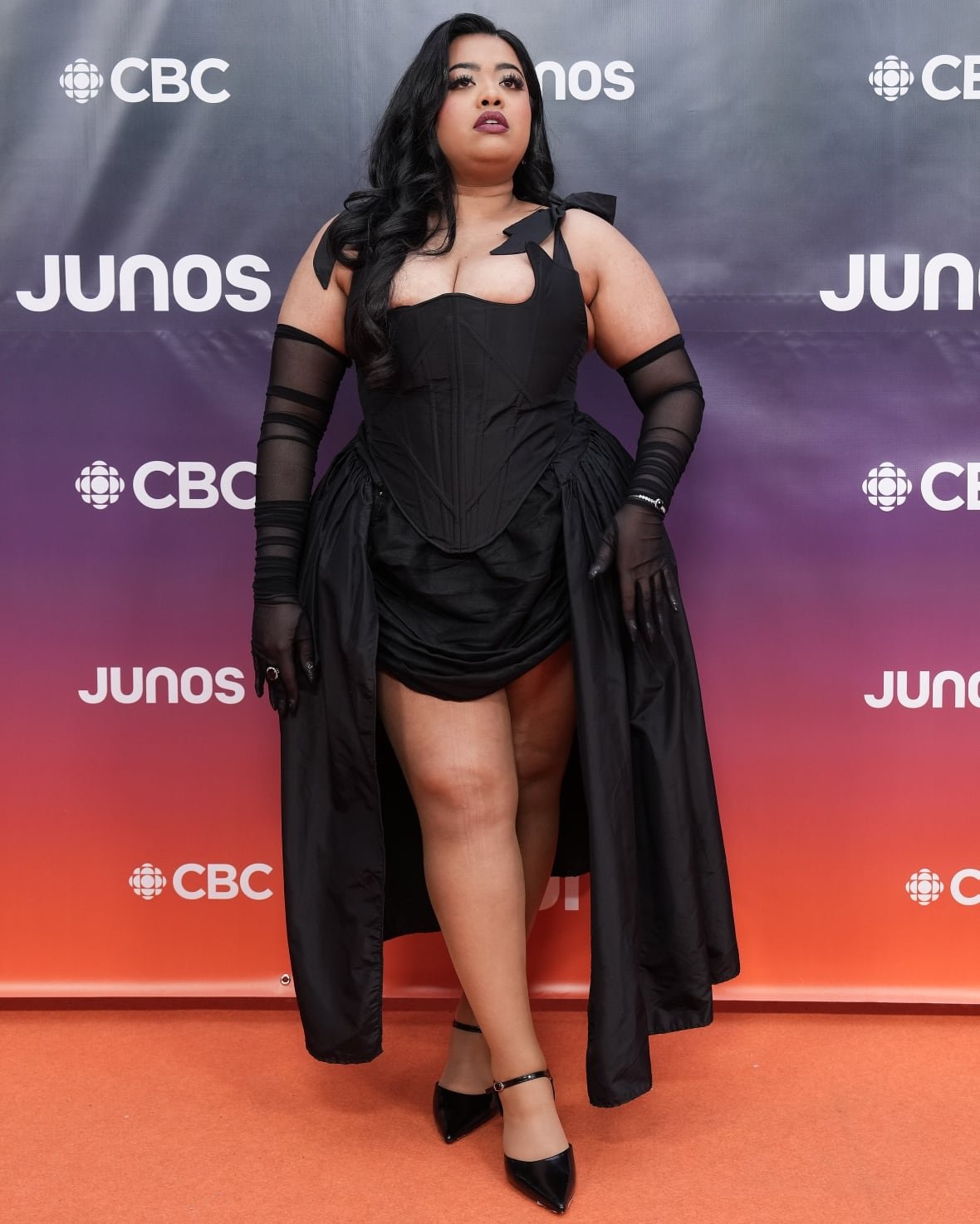 Benita on the red carpet wearing a black dress, sheer long gloves and black shoes.