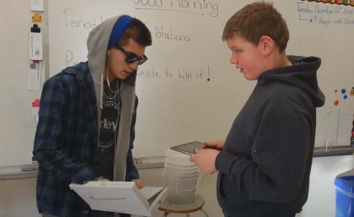 A young man hands an IPad to a youth.