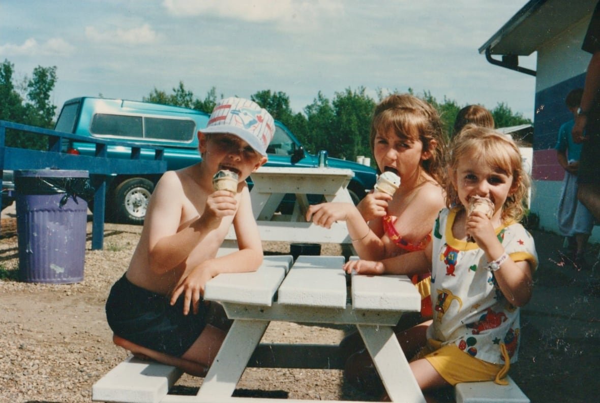 brett-howard-and-siblings Three children in summer clothes eating ice cream at a picnic table.