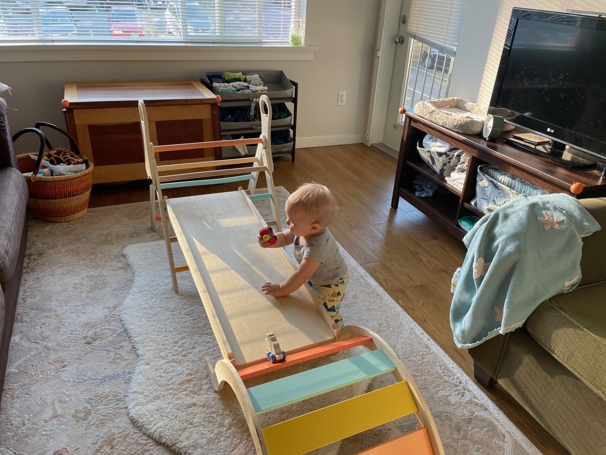 brett-howard-s-son A blond child holds a toy car while playing with a wooden indoor climbing set inside a living room.
