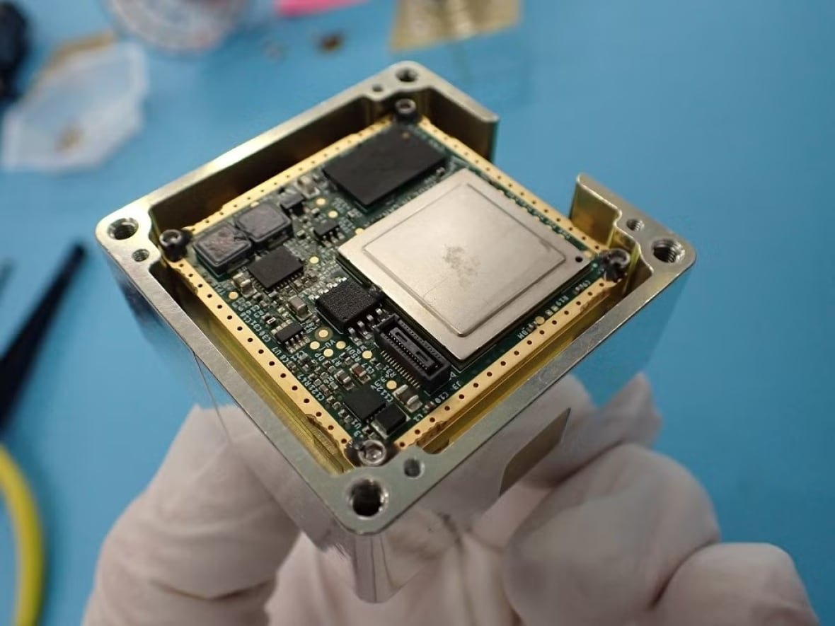 canadensys-chip A hand in a glove holds a square microchip inside a metal casing.
