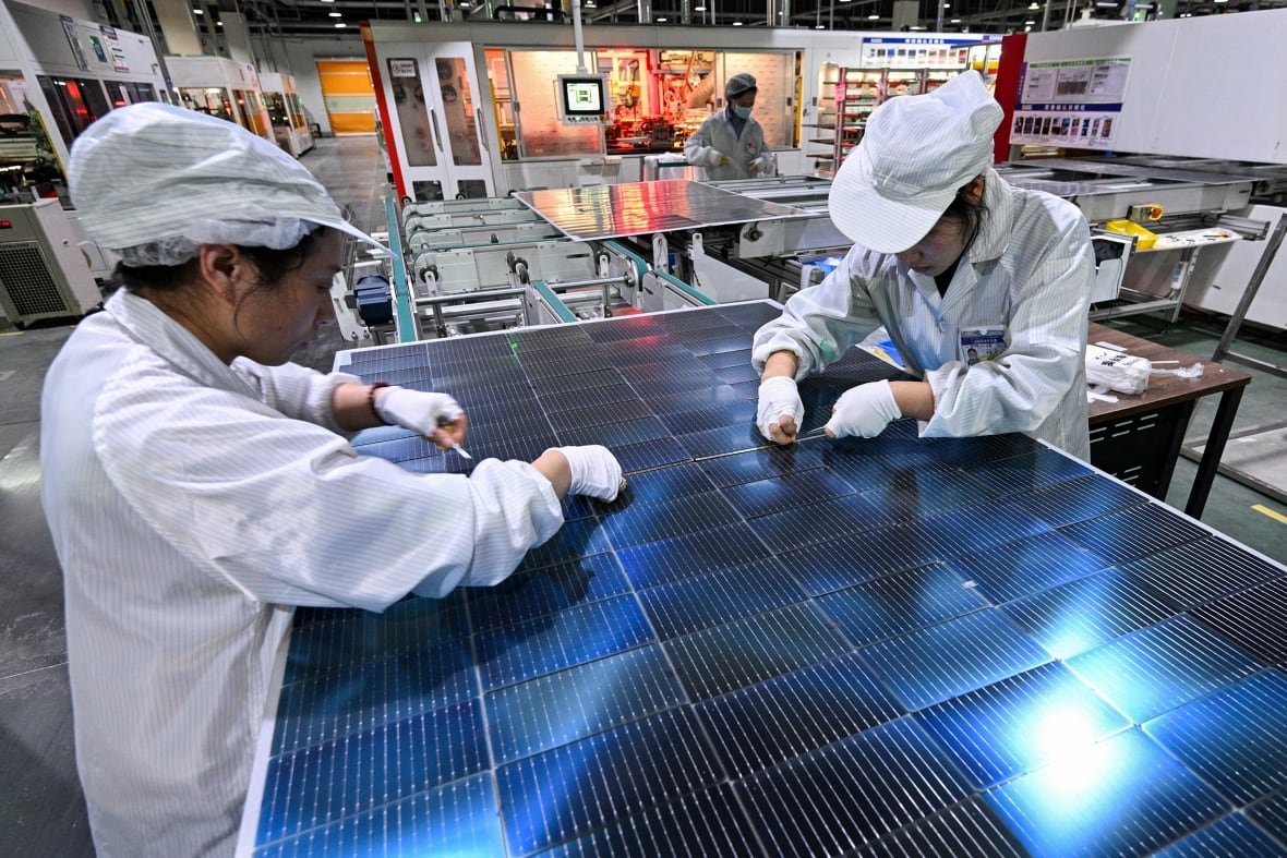 china-manufacturing-1 People with white uniforms lean over a solar panel