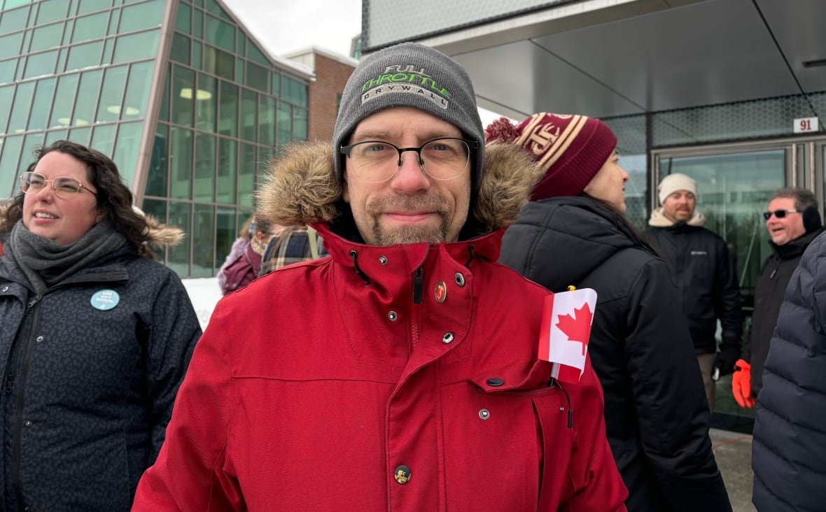 christian-latour A person in a winter hat and jacket stands before a crowd outside.